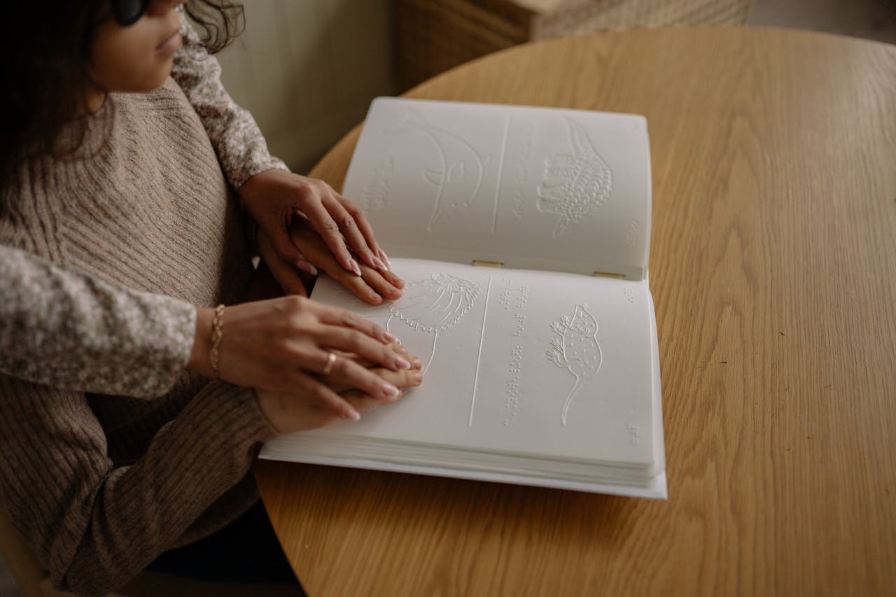 A child reads a Braille book with guidance, focusing on learning and touch.